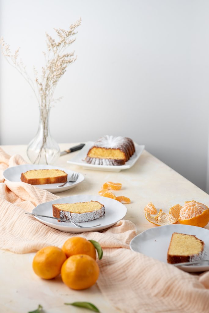 A scene with flowers, mandarines and slices of mandarin pound cake. 